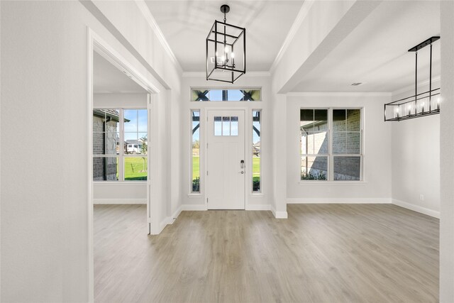 entryway with wood finished floors, an inviting chandelier, baseboards, and ornamental molding