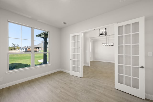 empty room featuring french doors, baseboards, light wood-type flooring, and a chandelier