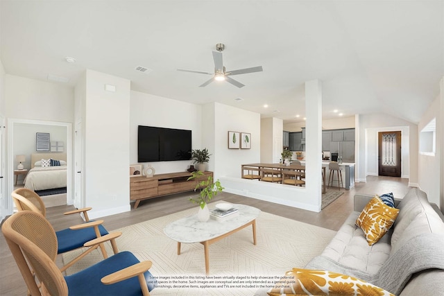 living room featuring light wood finished floors, visible vents, baseboards, and ceiling fan