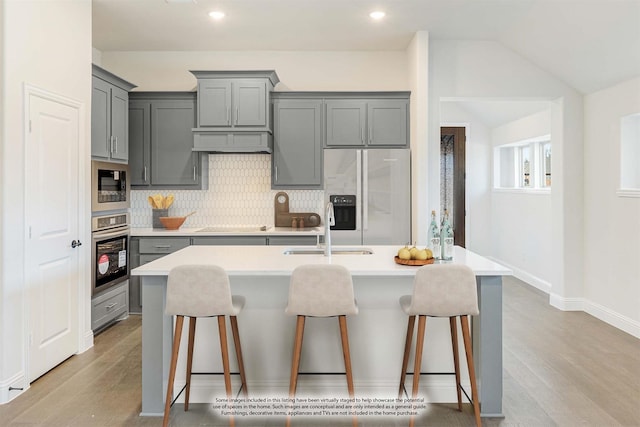 kitchen with a sink, gray cabinets, a kitchen bar, and stainless steel appliances