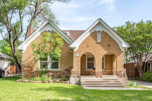 825 Thomasson Dr, Dallas, TX 75208 - tudor home with covered porch, a front yard, fence, brick siding, and a chimney
