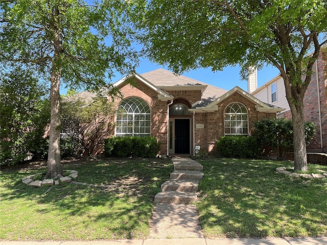 view of front of home with a front yard, brick siding, and roof with shingles