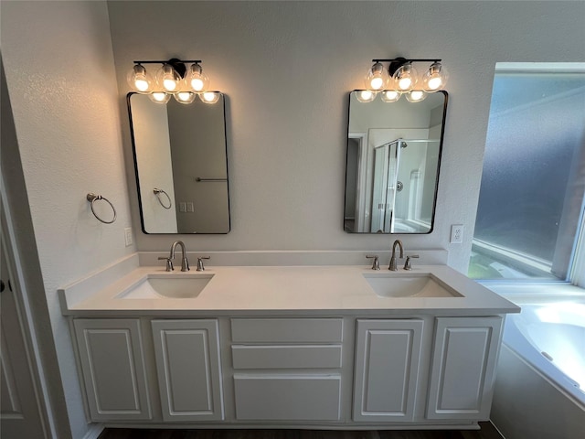 bathroom featuring a shower with shower door, double vanity, a bath, and a sink