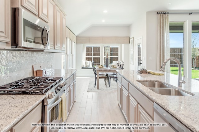 kitchen featuring tasteful backsplash, appliances with stainless steel finishes, light stone countertops, lofted ceiling, and a sink
