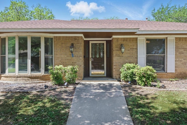 view of exterior entry with brick siding and a shingled roof