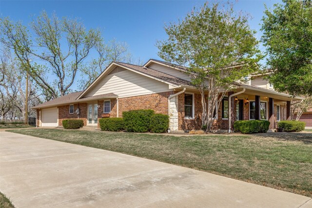 view of front facade with driveway, an attached garage, brick siding, french doors, and a front lawn