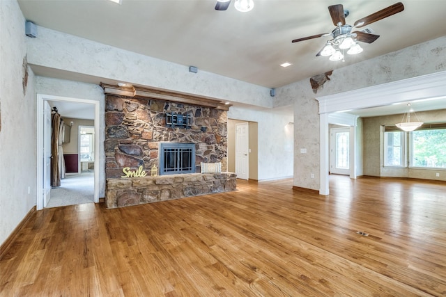 unfurnished living room featuring baseboards, wood finished floors, a ceiling fan, and a stone fireplace