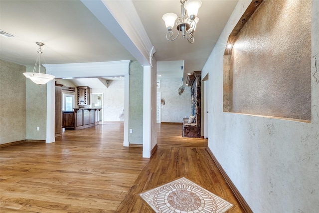 corridor featuring light wood finished floors, a notable chandelier, a textured wall, and visible vents