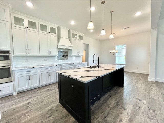 kitchen featuring tasteful backsplash, visible vents, a notable chandelier, stainless steel double oven, and custom range hood