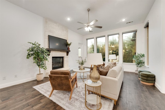 living room with ceiling fan, a stone fireplace, baseboards, dark wood-type flooring, and visible vents