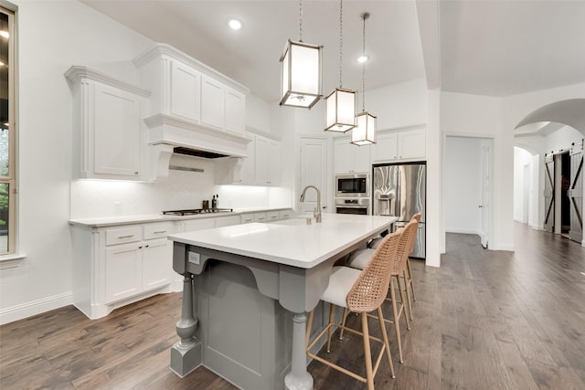 kitchen with a kitchen island with sink, a kitchen breakfast bar, light countertops, arched walkways, and stainless steel appliances