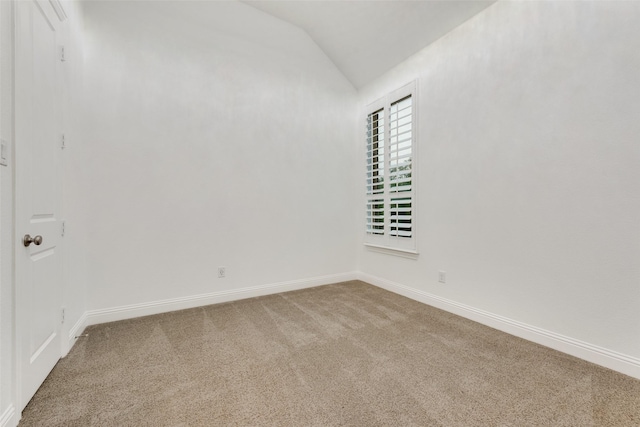 carpeted empty room featuring baseboards and vaulted ceiling