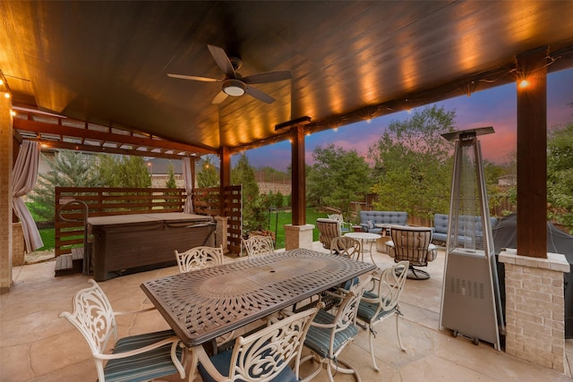 patio terrace at dusk with ceiling fan, a hot tub, an outdoor hangout area, and outdoor dining space