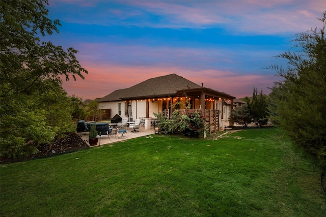 rear view of property with a lawn, a patio area, and stucco siding