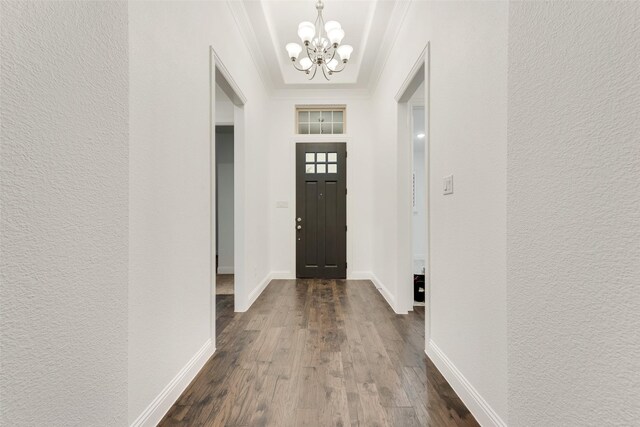 foyer entrance with a textured wall, an inviting chandelier, ornamental molding, baseboards, and dark wood-style floors