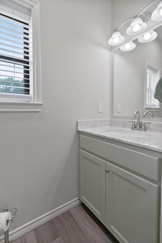 bathroom with baseboards, wood finished floors, vanity, and plenty of natural light