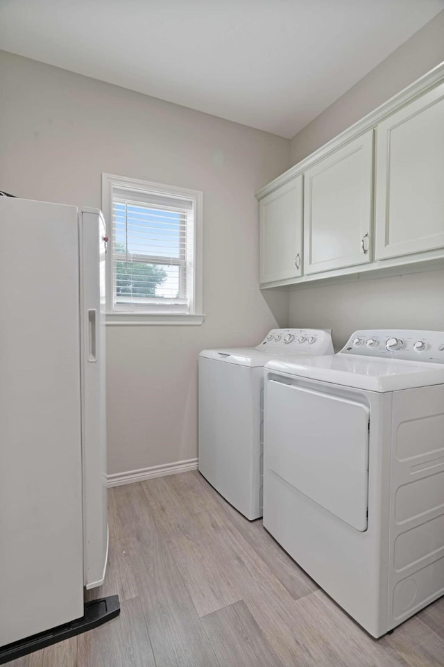laundry room featuring washing machine and dryer, cabinet space, baseboards, and light wood-style floors