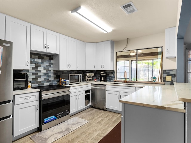 kitchen with tasteful backsplash, a sink, a peninsula, appliances with stainless steel finishes, and visible vents