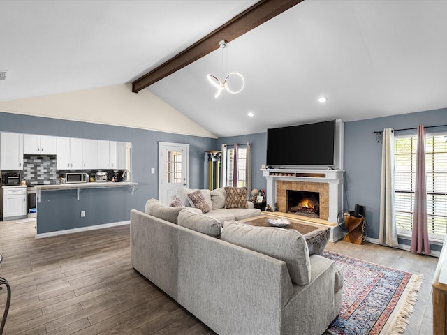 living room with a tiled fireplace, vaulted ceiling with beams, wood finished floors, and a wealth of natural light
