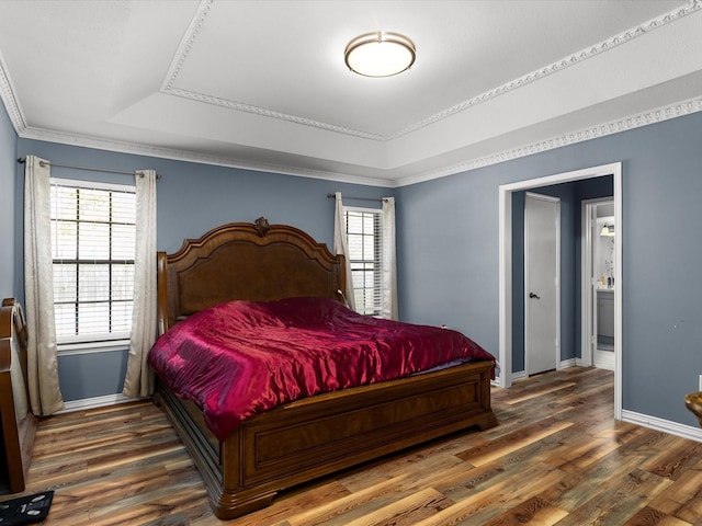 bedroom featuring wood finished floors, baseboards, a raised ceiling, and crown molding