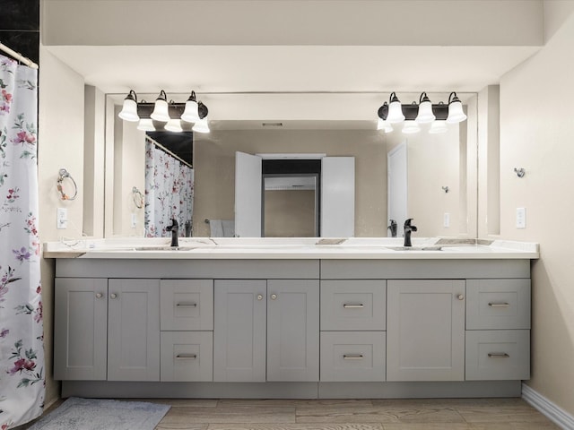 bathroom featuring wood finished floors, baseboards, a sink, and double vanity