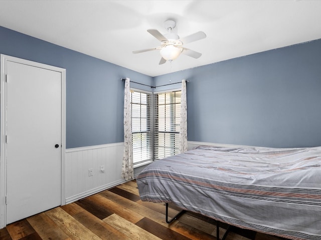 bedroom featuring wood finished floors, ceiling fan, and wainscoting