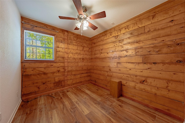 empty room with wooden walls, baseboards, a ceiling fan, and wood finished floors