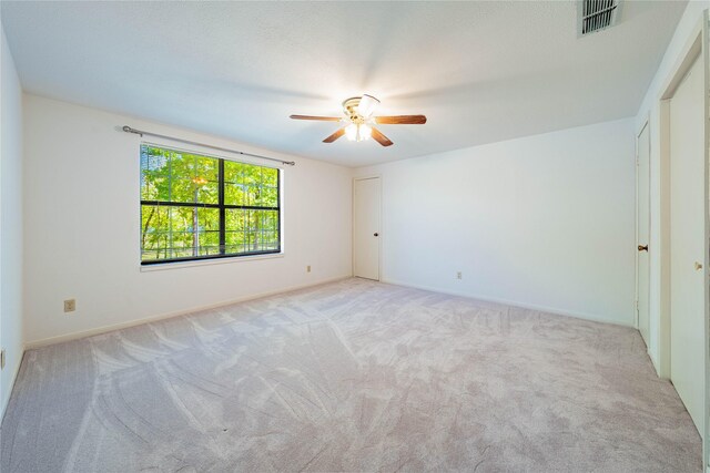 unfurnished bedroom featuring baseboards, visible vents, light colored carpet, and a ceiling fan
