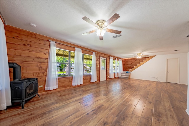 unfurnished living room with plenty of natural light, hardwood / wood-style flooring, a wood stove, and ceiling fan