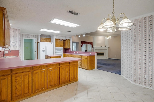kitchen featuring wallpapered walls, visible vents, a sink, white appliances, and a peninsula