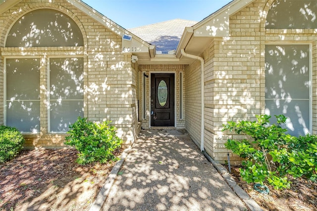 entrance to property featuring brick siding and roof with shingles