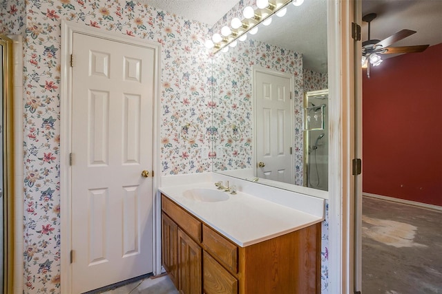 full bath featuring a shower stall, a ceiling fan, a textured ceiling, wallpapered walls, and vanity