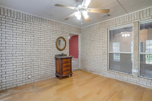 spare room with brick wall, wood finished floors, and ceiling fan
