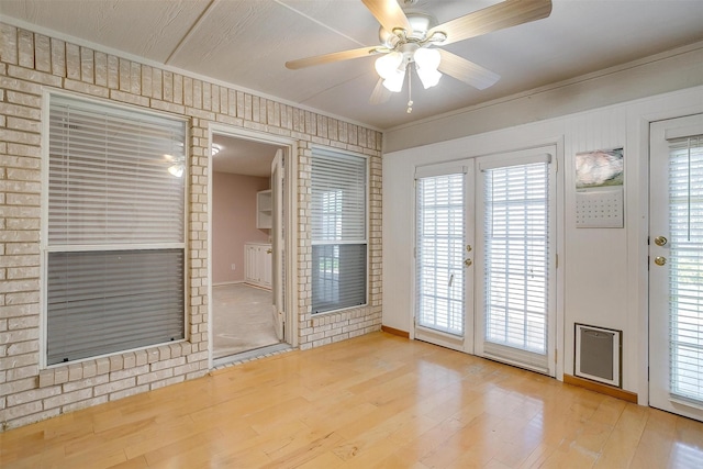 empty room with wood finished floors, a ceiling fan, french doors, a wealth of natural light, and crown molding