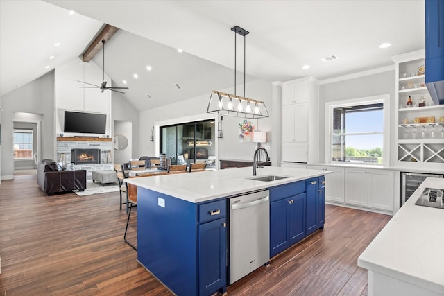 kitchen featuring stainless steel dishwasher, a sink, a warm lit fireplace, beam ceiling, and blue cabinetry