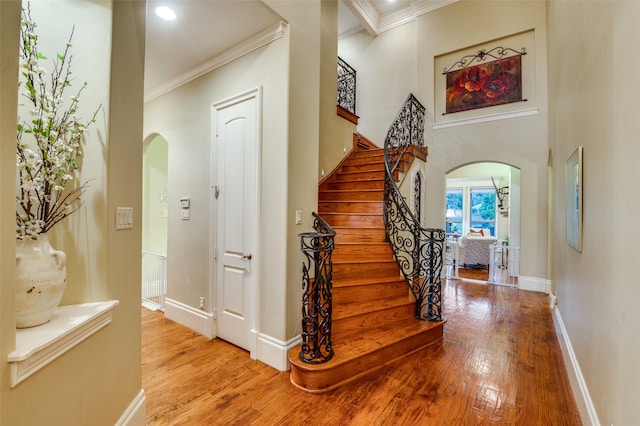 entryway with arched walkways, light wood-type flooring, ornamental molding, baseboards, and stairs