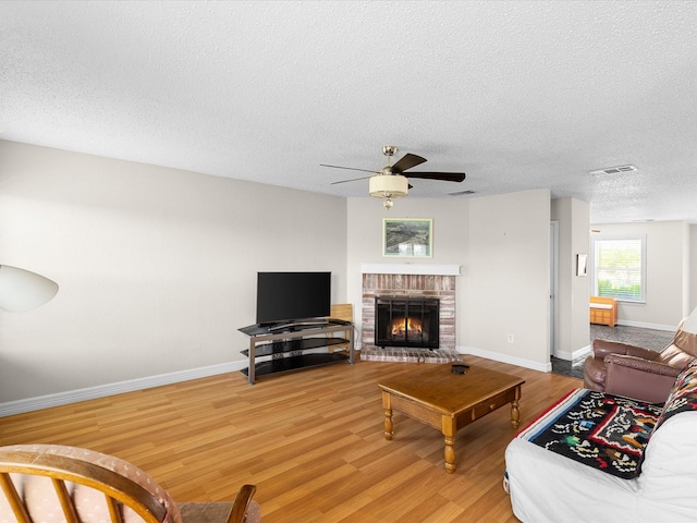 living area featuring baseboards, light wood-style flooring, a ceiling fan, a brick fireplace, and visible vents