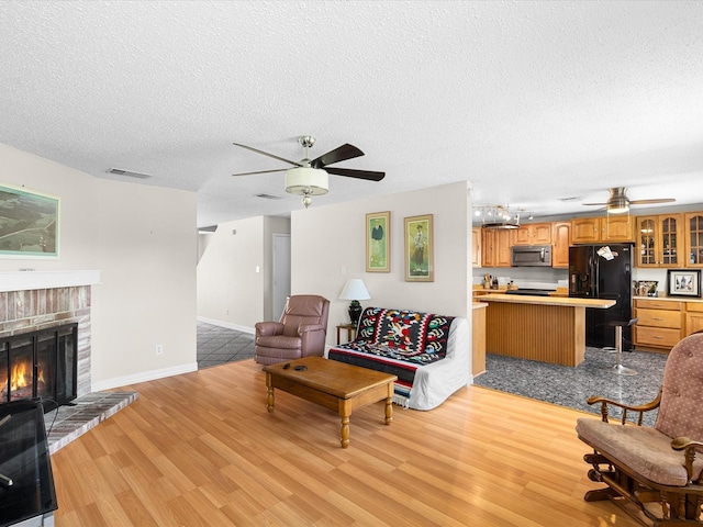 living room with light wood finished floors, a textured ceiling, ceiling fan, and a fireplace