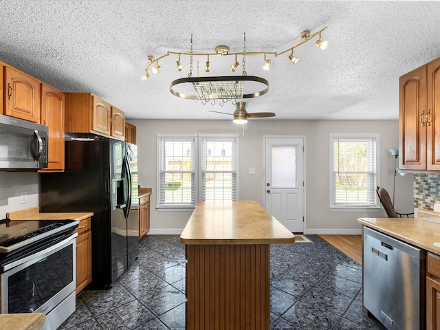 kitchen featuring baseboards, a center island, light countertops, a ceiling fan, and appliances with stainless steel finishes