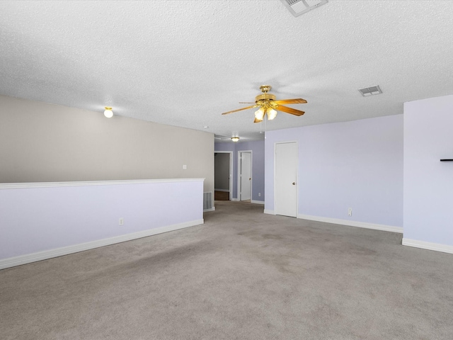 carpeted empty room featuring a textured ceiling, baseboards, a ceiling fan, and visible vents