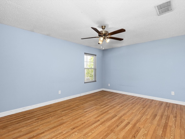 empty room with ceiling fan, light wood-type flooring, a textured ceiling, visible vents, and baseboards
