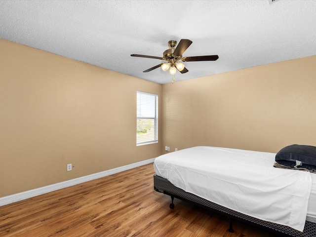 bedroom with light wood-style flooring, a textured ceiling, baseboards, and a ceiling fan