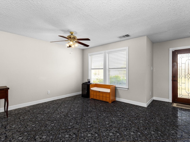 foyer featuring visible vents, baseboards, a ceiling fan, and a textured ceiling