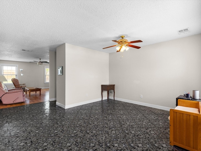 empty room featuring a textured ceiling, a ceiling fan, visible vents, granite finish floor, and baseboards