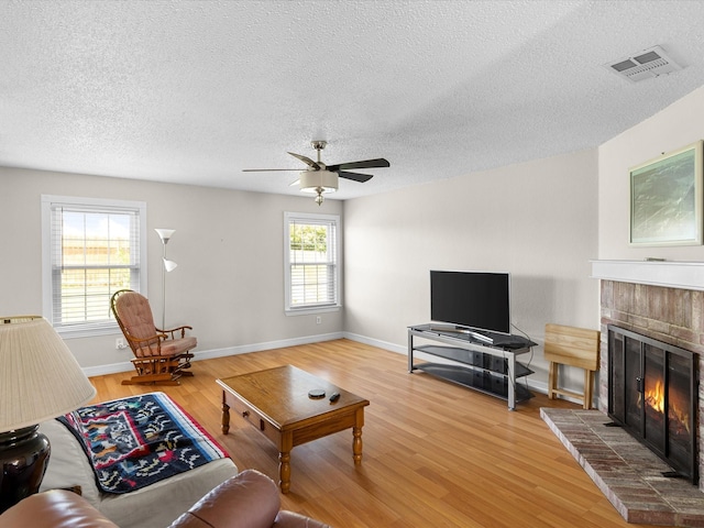 living room featuring visible vents, a ceiling fan, a textured ceiling, a fireplace, and wood finished floors
