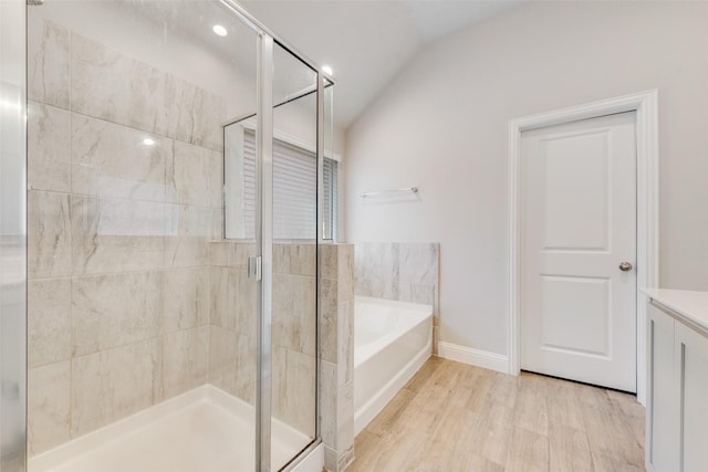 bathroom with a shower stall, vaulted ceiling, wood finished floors, a bath, and baseboards