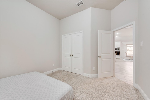 bedroom featuring a closet, visible vents, light colored carpet, and baseboards