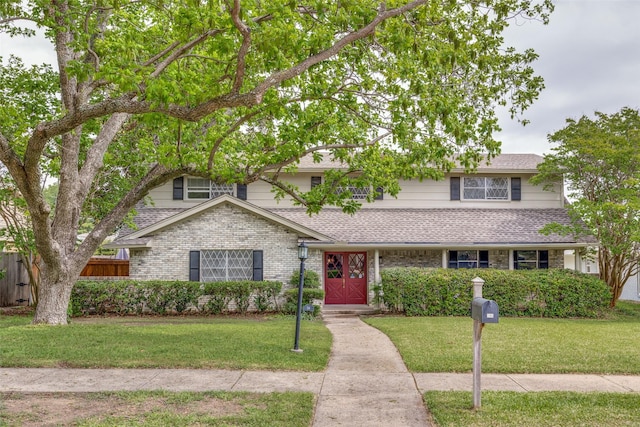 traditional-style home featuring fence, roof with shingles, brick siding, and a front lawn