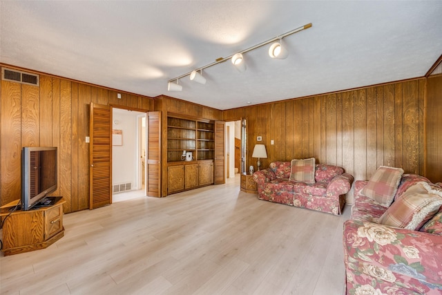 living area featuring rail lighting, wooden walls, visible vents, and wood finished floors