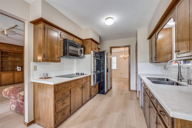 kitchen featuring black appliances, a sink, brown cabinetry, and light wood-style floors